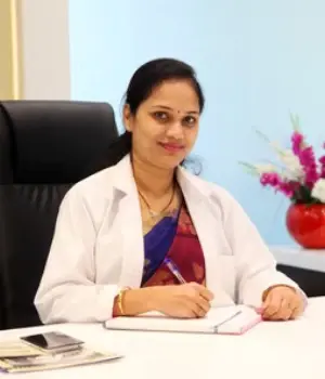 Female doctor in saree and white coat writing in notebook at clinic desk – patient-friendly setup