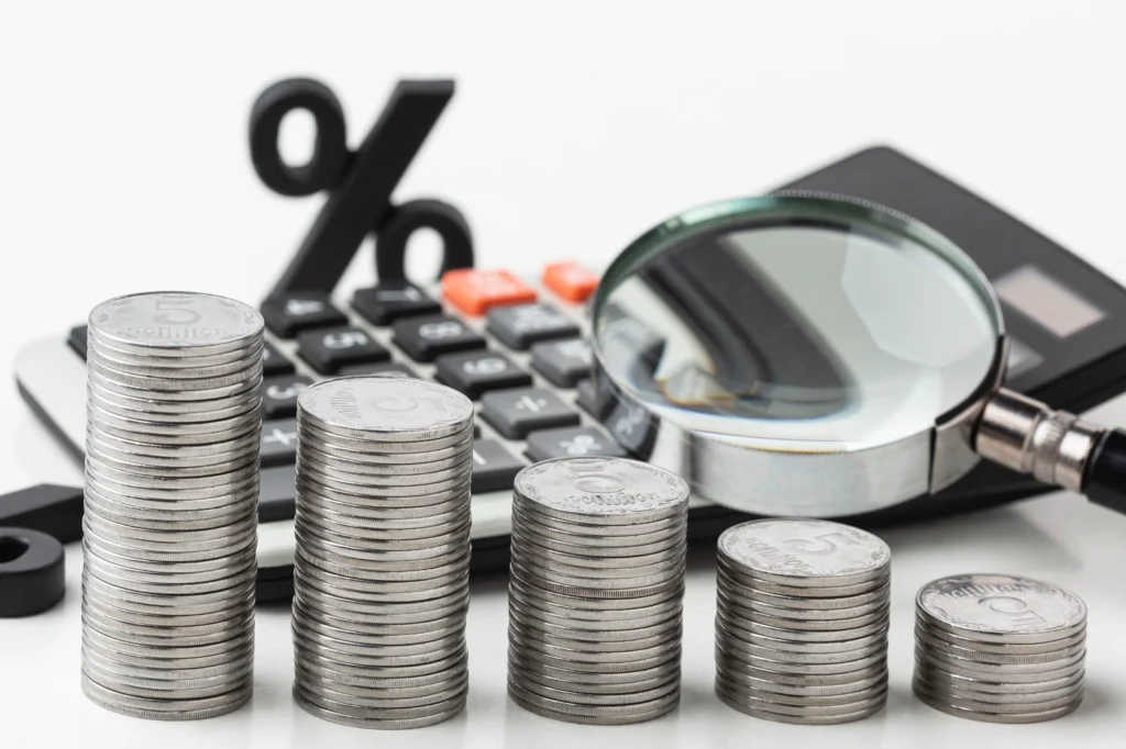 Stacks of coins with a calculator and magnifying glass in the background, symbolizing financial analysis or investment in healthcare